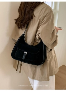 Macro detail of black suede crescent bag with silver buckle flap in minimalist room
