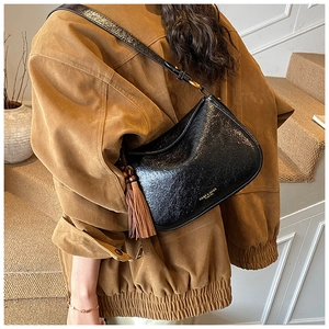 Detail of glossy black leather shoulder bag with brown tassel and embossed fashion text