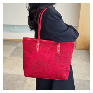 Detail of red tote bag featuring 3D floral embroidery and gold rivets on the shoulder strap