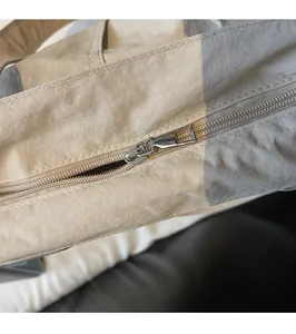 Détail de la fermeture éclair argentée et du tissu en nylon beige d'un grand cabas