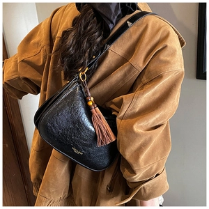 Detail of black semi-circle bag with vintage texture and brown wood bead tassel