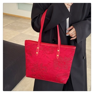 Detail of red tote bag with floral jacquard texture held by model in black suit