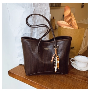 Detail of dark brown woven tote bag with fashion text and vintage wooden bead charm