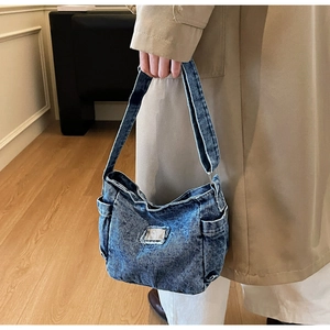Détail du sac d'épaule en denim avec poche latérale et logo métal sur tissu délavé