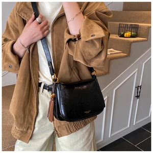 Detail of black oil wax leather crossbody bag featuring brown tassels and gold hardware
