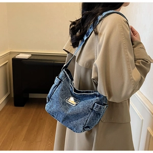 Détail du sac à bandoulière en denim bleu avec large sangle et accent métallique