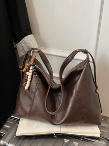 Brown vintage faux leather tote bag with wooden bead charm on a silver suitcase
