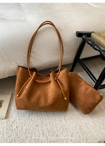 Detail view of a brown suede tote bag and zipper pouch set on a white rug