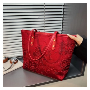 Macro shot of red tote bag featuring jacquard floral patterns and golden metal rivets