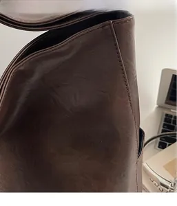 Gros plan sur la texture du cuir marron foncé et les coutures d'un sac cabas vintage