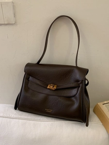 Retro dark brown leather shoulder bag with brass buckle on a minimalist sofa background