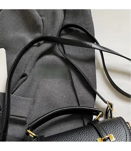 Close-up of black lychee grain leather handbag with gold metal clasp on gray fabric