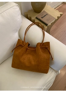 Detail of caramel suede tote bag with slim handles and golden beads on a white sofa
