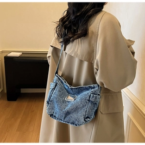 Detail of retro blue denim shoulder bag with frayed edges and metal label on model