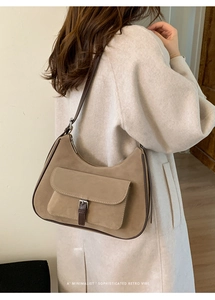 Detail of a brown suede half-moon shoulder bag with retro buckle strap and leather piping