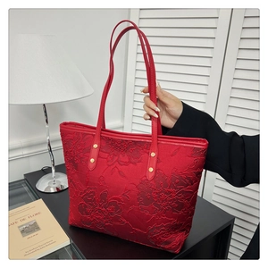 Macro view of red tote bag featuring 3D floral embroidery and gold rivet details