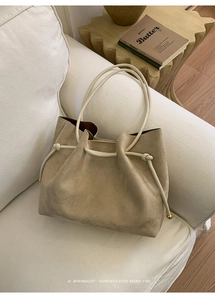 Detail of beige suede tote bag with leather handles and gold orb metallic hardware