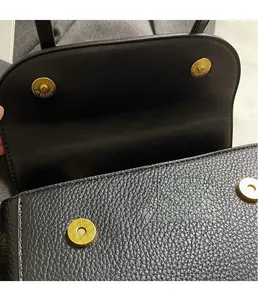 Detailed macro view of the gold magnetic buckle on a vintage black pebbled leather bag