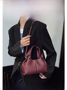 Détail d'un sac seau plissé en cuir bordeaux avec garnitures argentées sur un tailleur
