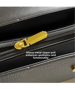 Detail of a polished gold-tone metal zipper pull on a black textured leather bag