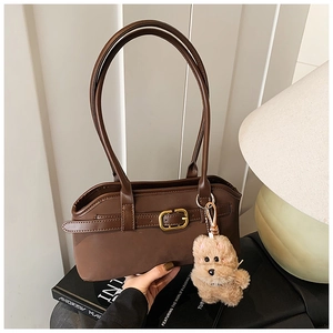 Detail der braunen Vintage-Schultertasche mit Goldschnalle und Plüschhund auf Kunstbüchern