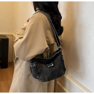 Detail of gray washed denim crossbody bag featuring a side pocket and metal plaque