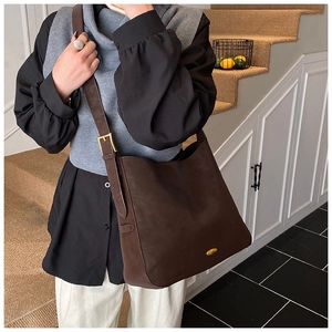 Detail of dark brown tote bag showing gold oval buckle and adjustable wide shoulder strap