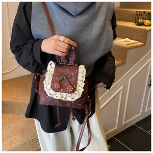 Détail d'un sac à dos rétro marron avec bordure en dentelle et breloques cerise