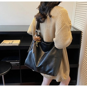 Détail d'un sac cabas en cuir noir avec un charm ours marron et des textures souples