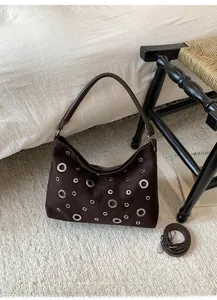 Detailed shot of dark brown suede shoulder bag with silver eyelets on a woven chair