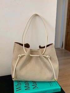 Minimalist beige suede tote bag with golden drawstring details on a blue book