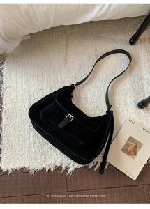 Detail of a black matte hobo bag with a silver buckle on a cozy white fringed rug