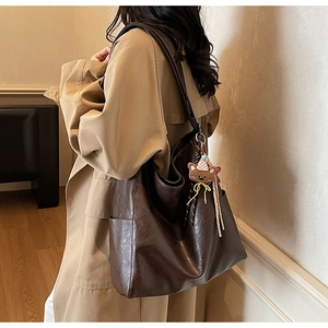 Detail view of large dark brown leather tote bag with a cute bear keychain charm
