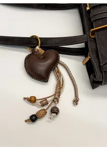 Close-up of heart-shaped dark brown leather bag pendant with woven ropes and wooden beads