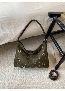 Detail of dark green suede shoulder bag with silver eyelets on a soft white bed