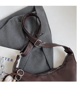 Détail du sac en cuir marron foncé avec surpiqûres blanches et breloque baseball