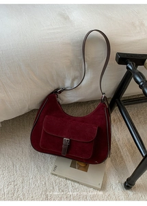 Detail of burgundy suede hobo bag with front flap pocket and brown leather trim on a magazine