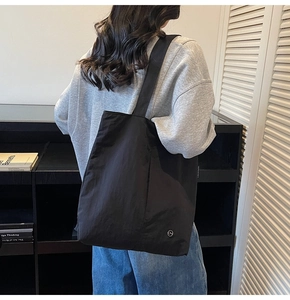 Gros plan du sac cabas noir en nylon imperméable avec logo CM porté par un mannequin urbain