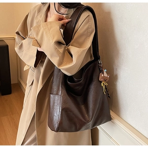 Gros plan d'un sac hobo marron foncé avec charme d'ours sur un trench kaki