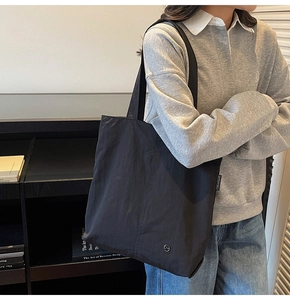 Détail du fourre-tout noir en nylon imperméable montrant les coutures et le logo sur l'épaule