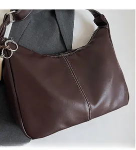 Détail d'un sac seau marron foncé avec surpiqûres blanches contrastées et anneau métallique