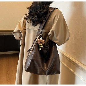 Close-up of a large brown leather tote bag with a cute plush bear charm on the shoulder strap