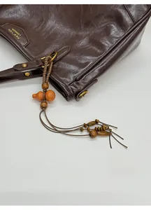 Detail of dark brown leather tote with a wooden gourd pendant and gold logo imprint