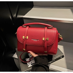 Detail of red leather satchel with lychee texture and gold metal buckle hardware