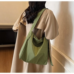 Detailed side view of green checkered oxford hobo bag worn by a model in a trench coat