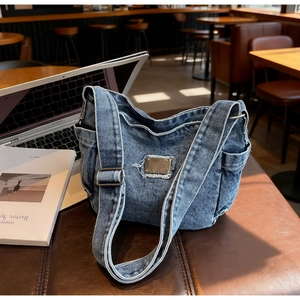 Détail d'un sac bandoulière en denim avec plaque métallique et poches latérales bleues