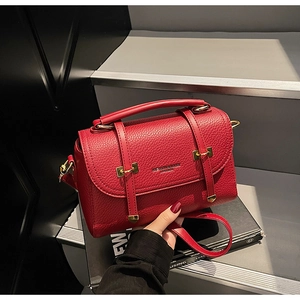 Detailed view of red lychee textured leather crossbody bag with golden buckles and top handle