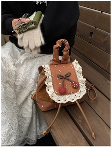 Détail du sac à dos vintage marron avec bordure en dentelle et pendentif cerise
