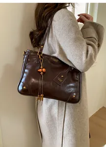 Detail of dark brown glossy leather tote with gold hardware and beaded tassel charm