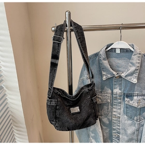 Detail of a vintage washed black denim crossbody bag with side pocket and metal hardware